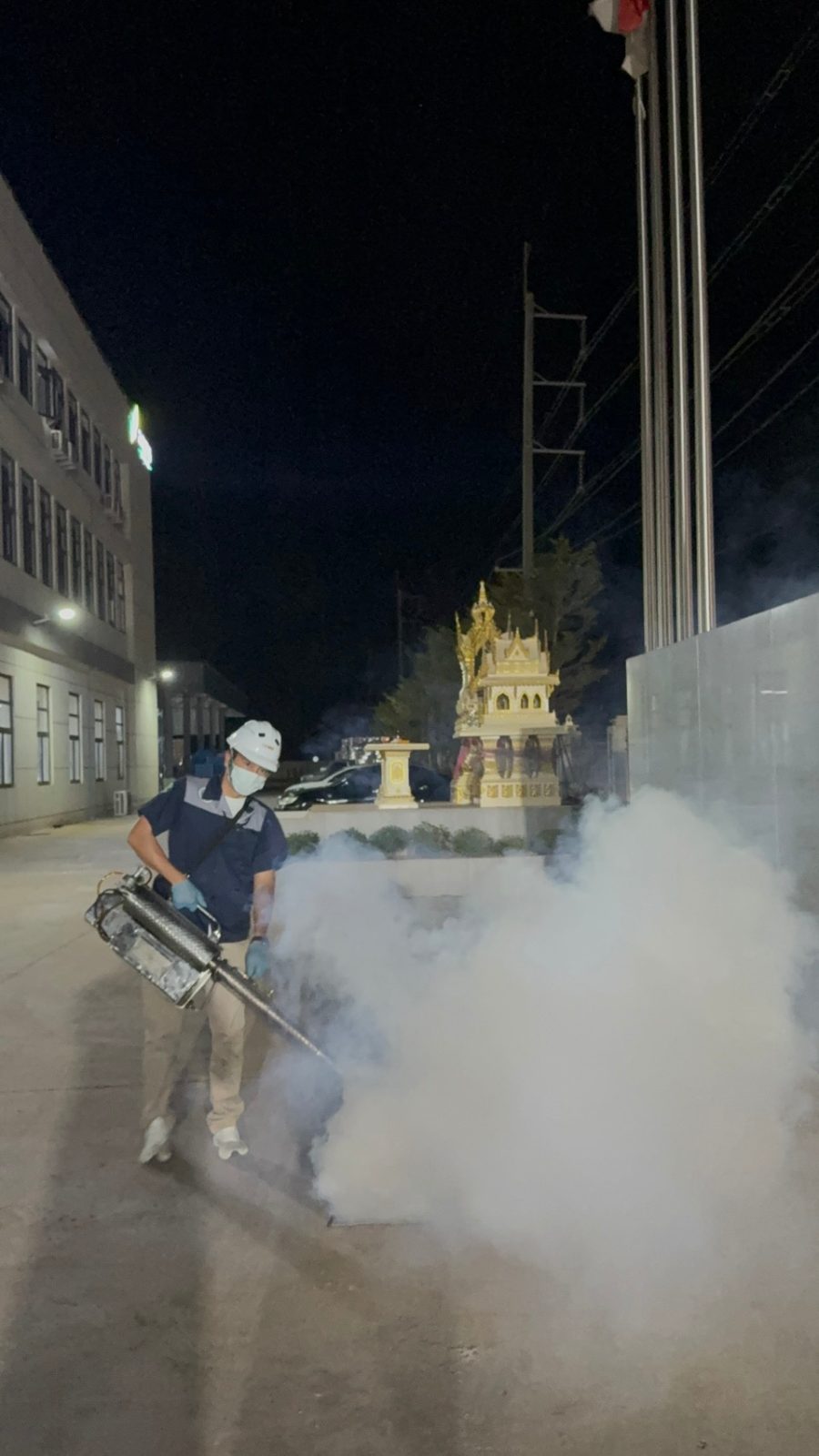 เจ้าหน้าที่เริ่มขั้นตอนพ่นหมอกควัน (Thermal Fogging) บริเวณลานโล่งภายนอกอาคารยามค่ำคืน เพื่อลดปริมาณยุงรำคาญเต็มวัยตามหลัก IPM